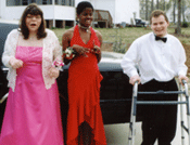 two girls in prom dresses with guy in tux using a walker